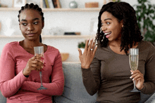 two women sitting on a couch drinking champagne