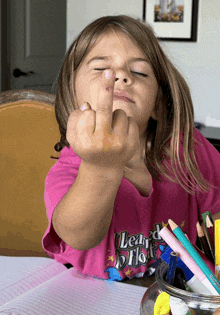 a little girl wearing a pink shirt that says " learn to float " giving the middle finger