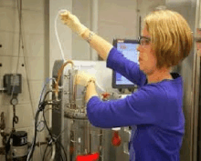 a woman wearing gloves and glasses is working on a machine in a lab .