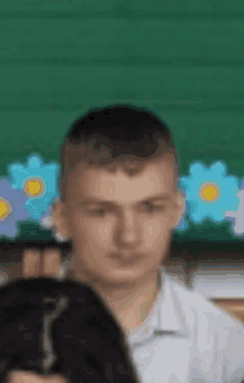 a young man in a white shirt is sitting in front of a green board with flowers on it .