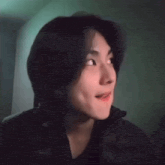a young man with long black hair is wearing a black jacket and smiling .