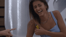 a woman in a blue tank top is laughing and holding a yellow object