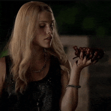 a woman in a black top is holding a piece of meat in her hand covered in blood