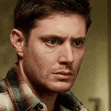 a close up of a man 's face with a plaid shirt on .