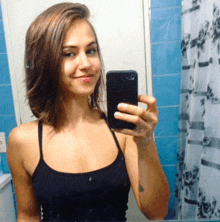 a woman in a black tank top takes a selfie in front of a mirror