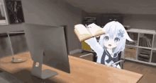 an anime girl is sitting at a desk with a computer and holding an open book