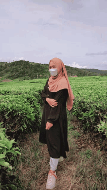 a woman wearing a mask stands in a field of green plants