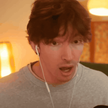 a man wearing ear buds and a gray shirt looks surprised