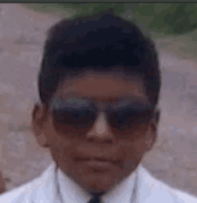 a close up of a young boy wearing sunglasses and a white suit .