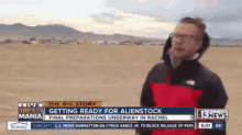 a man in a red and black jacket is standing in front of a sign that says the big story