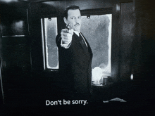 a black and white photo of a man pointing a gun with the words " don 't be sorry " below him