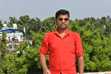 a man in a red shirt and sunglasses stands in front of a building