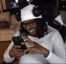 a man wearing a white hat and headphones is sitting in a chair looking at his phone .