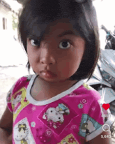 a little girl wearing a pink hello kitty shirt is looking at the camera