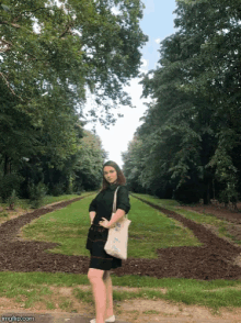 a woman in a black dress stands in a park holding a tote bag that says ' i love you ' on it