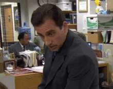 a man in a suit sits at a desk in front of a box that says ' nbc ' on it