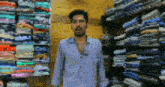 a man in a blue shirt is standing in front of a stack of shirts in a store .