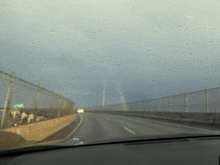 a car windshield with rain drops on it and a green sign on the right