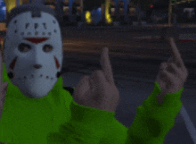 a person wearing a jason voorhees mask and a green hoodie is giving the middle finger