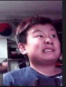 a young boy in a blue shirt is making a funny face while looking at the camera .