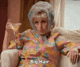 a woman sitting in a chair holding a martini with the words big hair written below her