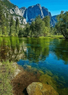 a lake surrounded by trees and mountains with a waterfall reflected in the water