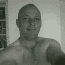 a black and white photo of a shirtless man taking a selfie with his phone .