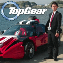 a man in a suit and tie stands in front of a red sports car that says topgear on it