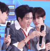 a man in a suit and tie is holding a microphone while two other men look on .