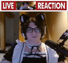 a man in a maid costume is sitting in front of a microphone with a live reaction sign above him .