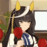 a girl with long black hair and yellow ears is holding two red boxing gloves in front of a television .