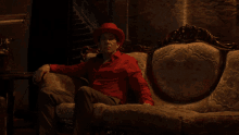 a man in a red hat sits on a couch in a dark room