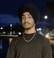 a man wearing a black turban and a gold chain looks at the camera