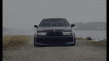 a black bmw is parked on a gravel road near the water
