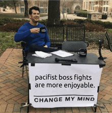 a man sits at a table with a sign that says " pacifist boss fights are more enjoyable change my mind "