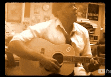 a man playing an acoustic guitar in front of a wall with a poster that says alex on it