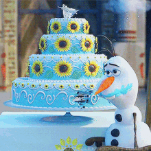 a cake with sunflowers on it is on a table next to a snowman