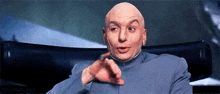 a bald man is sitting in a chair and pointing at the camera with his finger .