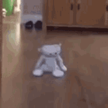 a white teddy bear is sitting on a wooden floor in a room .