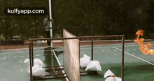 a man is standing in front of a fence on a tennis court while a fire is coming out of it .