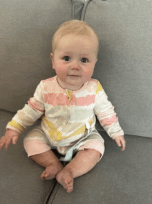 a baby is sitting on a couch wearing a tie dye onesie