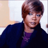 a woman wearing a purple shirt and a blue coat looks at the camera