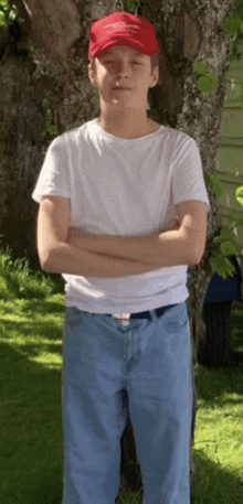 a young boy wearing a white shirt and a red hat stands with his arms crossed