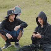 a man wearing a hat with a skull on it sits next to another man wearing a hoodie