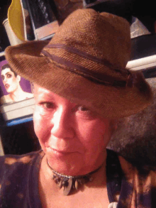 a woman wearing a straw hat and a choker looks at the camera