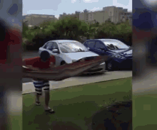 a man in a red shirt is carrying a large blanket in front of a car parked on the side of the road