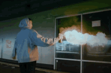 a person in a blue hoodie is spray painting a building