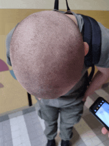 a man with a shaved head holds a cell phone in his hand