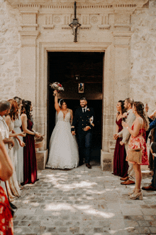 a bride and groom walk out of a church surrounded by their wedding party