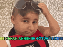 a young boy wearing sunglasses and a bib with the words bedirhan annenin gotunu sikeyi